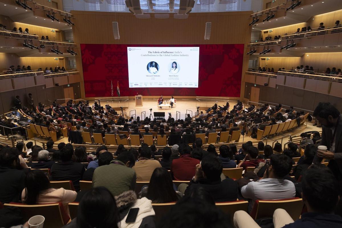 A packed, tiered auditorium facing a two-person conversation on stage
