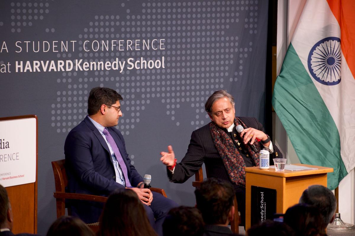 Two speakers in armchairs on stage, the Indian flag behind them